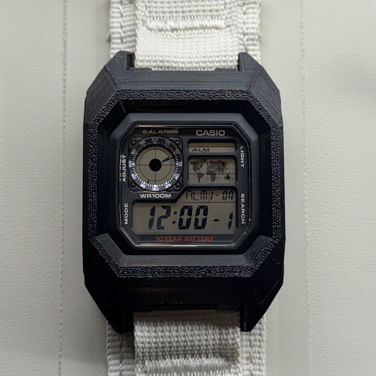 PROTOWORX AE1200 MOLLE Case in Stealth Black, mounted on MOLLE webbing with a Casio AE1200WH seated in the case